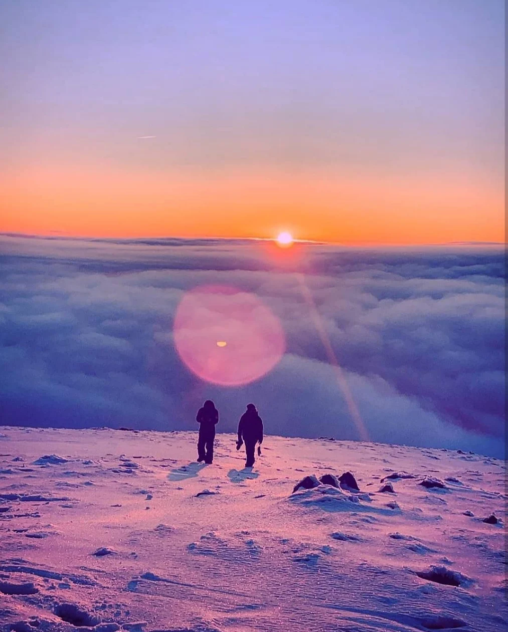 Two riders walking out across the snow at sunset, above a sea of cloud at Mt Hotham