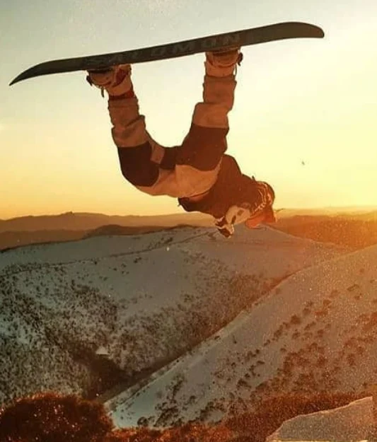 A snowboarder inverted mid-grab against the golden Mt Hotham sunset